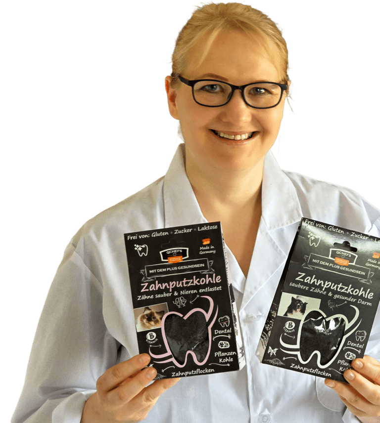 Anke Nagler Mikrobiologin im Kittel mit Brille lächelt und hält zwei Packungen QCHEFS Zahnputzkohle – natürliche Zahnpflege für Hunde und Katzen.